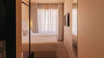 A hotel room with a large bed, a flat-screen TV, and a window with sheer curtains.