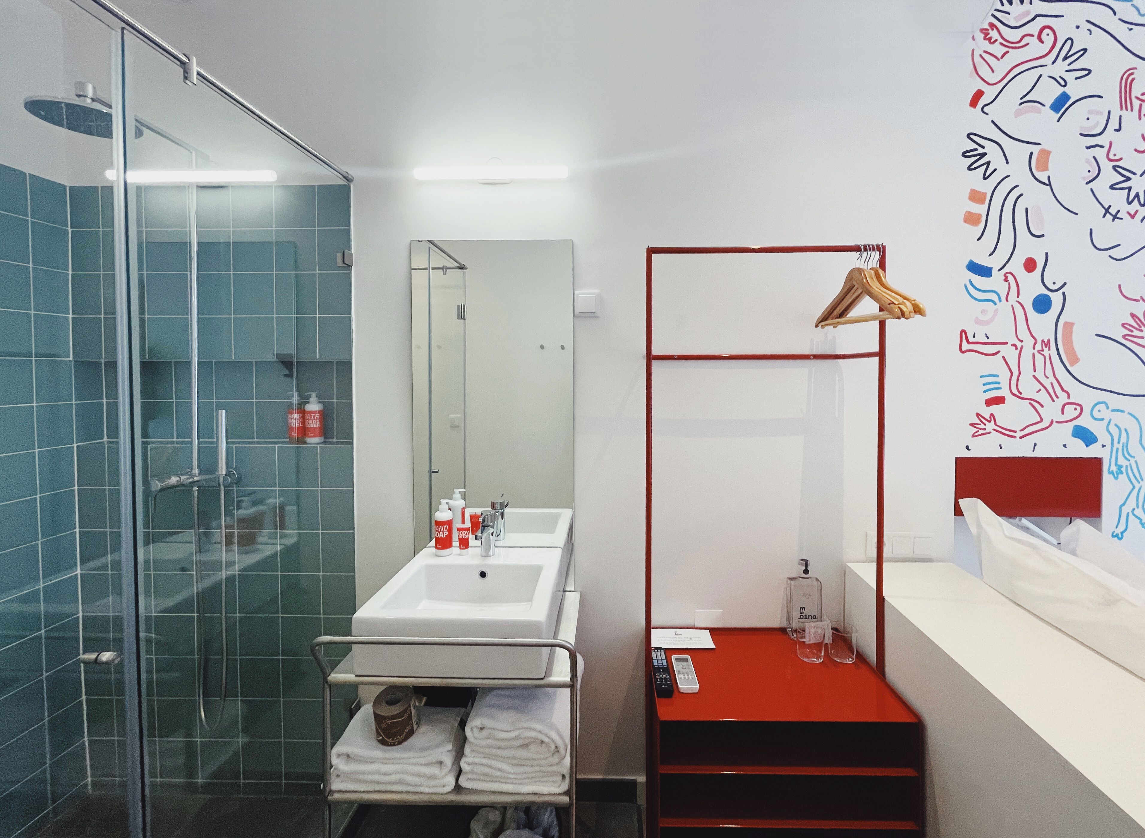 Un baño moderno con cabina de ducha de vidrio, un lavamanos blanco con espejo y un mueble de almacenamiento rojo.