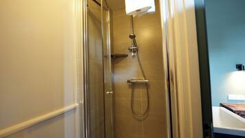 A glass-enclosed shower with a handheld showerhead, a towel hanging on the wall, and a white sink with a wooden countertop.