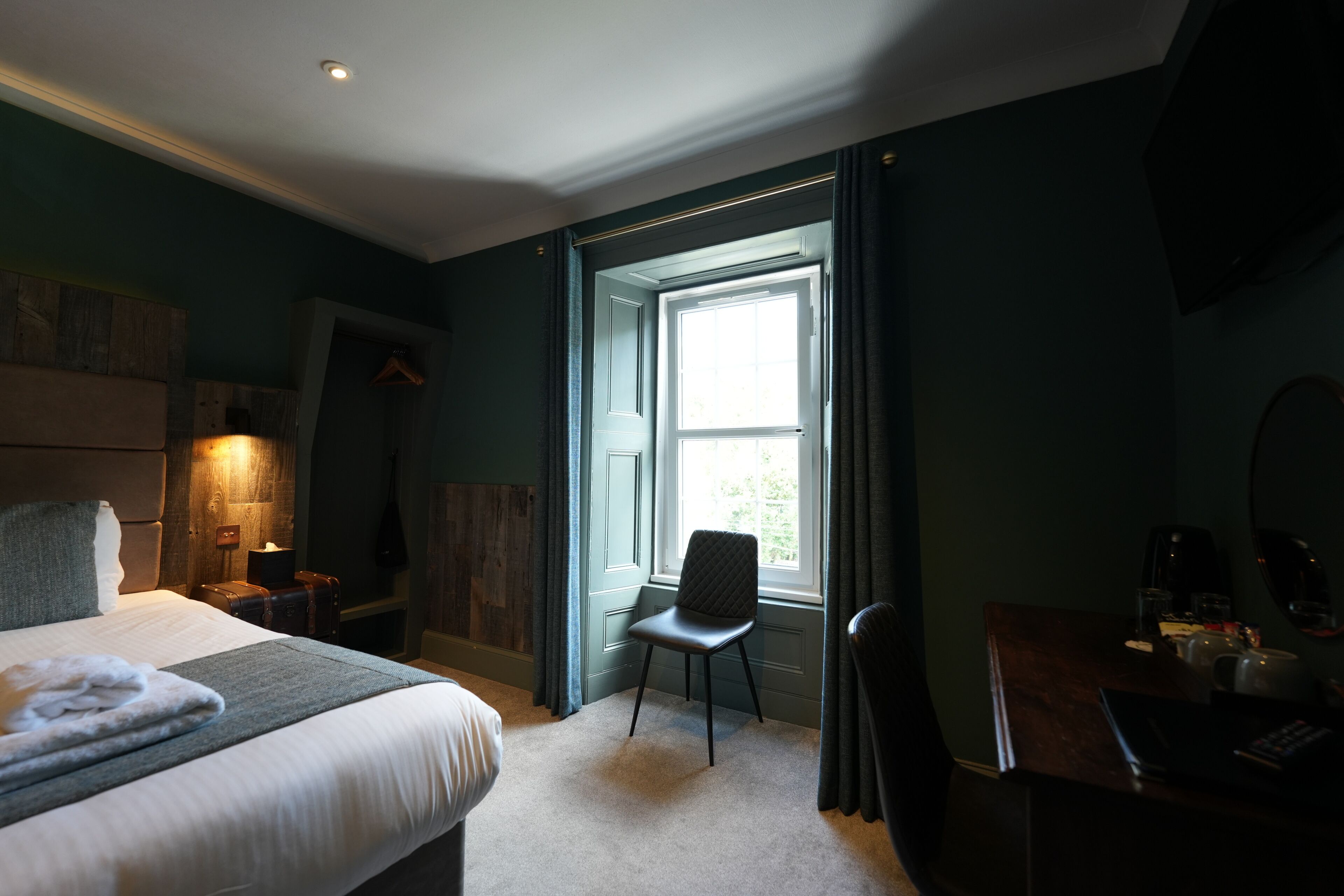 A hotel room with a bed, a desk, a chair, a window, and a shower area.
