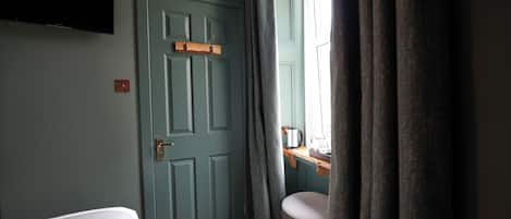 A room with a bed, a desk with a kettle, a window with curtains, and a door.