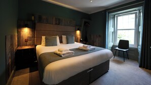 Quarto com uma cama grande, mesas de cabeceira, uma cadeira e uma janela com cortinas.