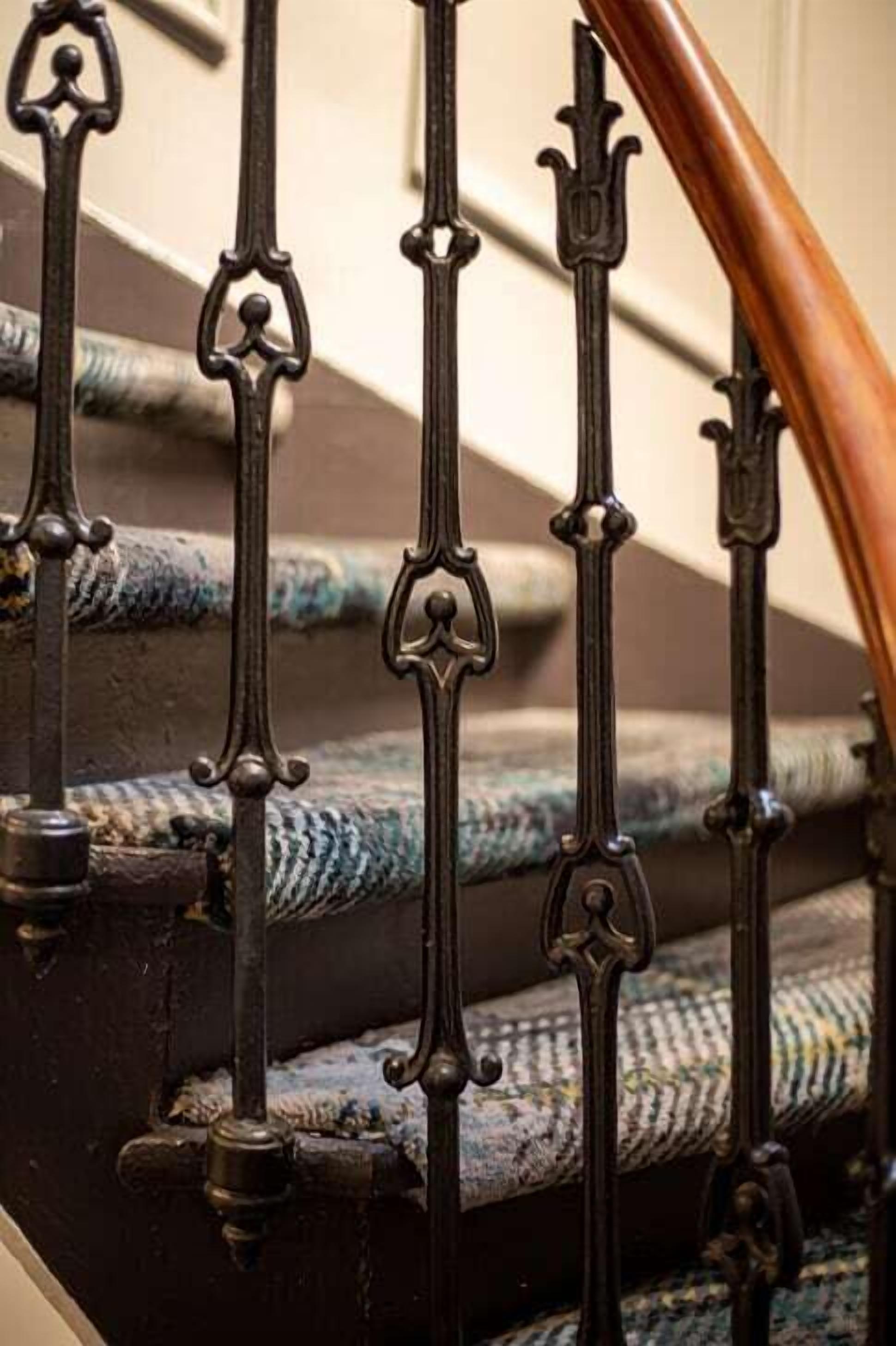 Uma escadaria com grades de metal preto ornamentadas e corrimão de madeira.