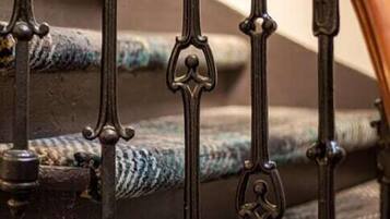 Uma escadaria com grades de metal preto ornamentadas e corrimão de madeira.