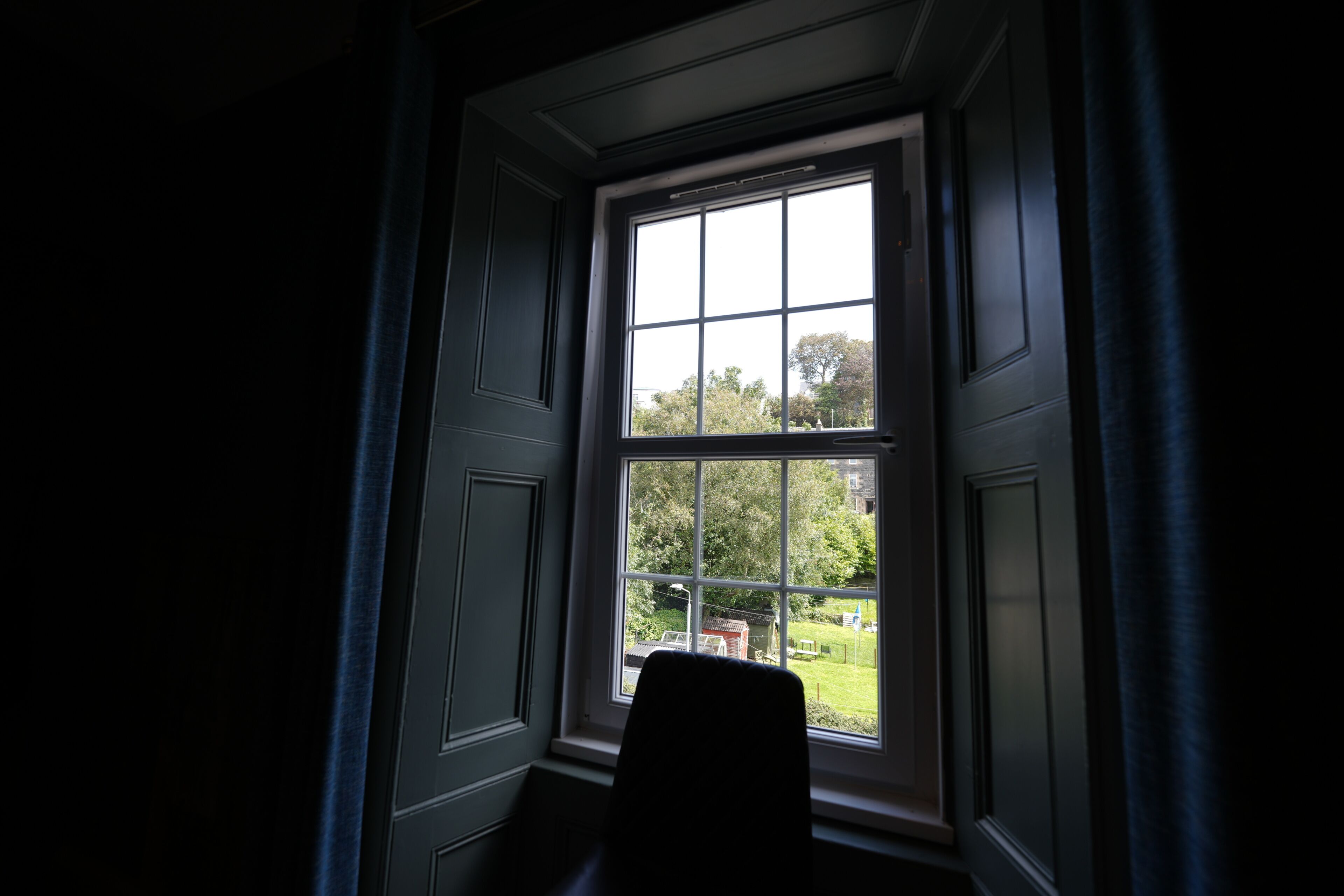 A room with a large window, a chair, and a view of greenery outside.