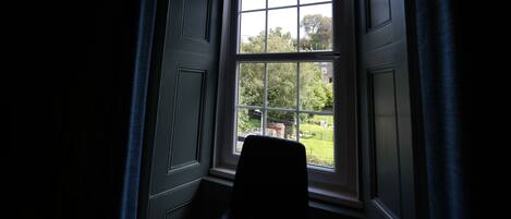A room with a large window, a chair, and a view of greenery outside.