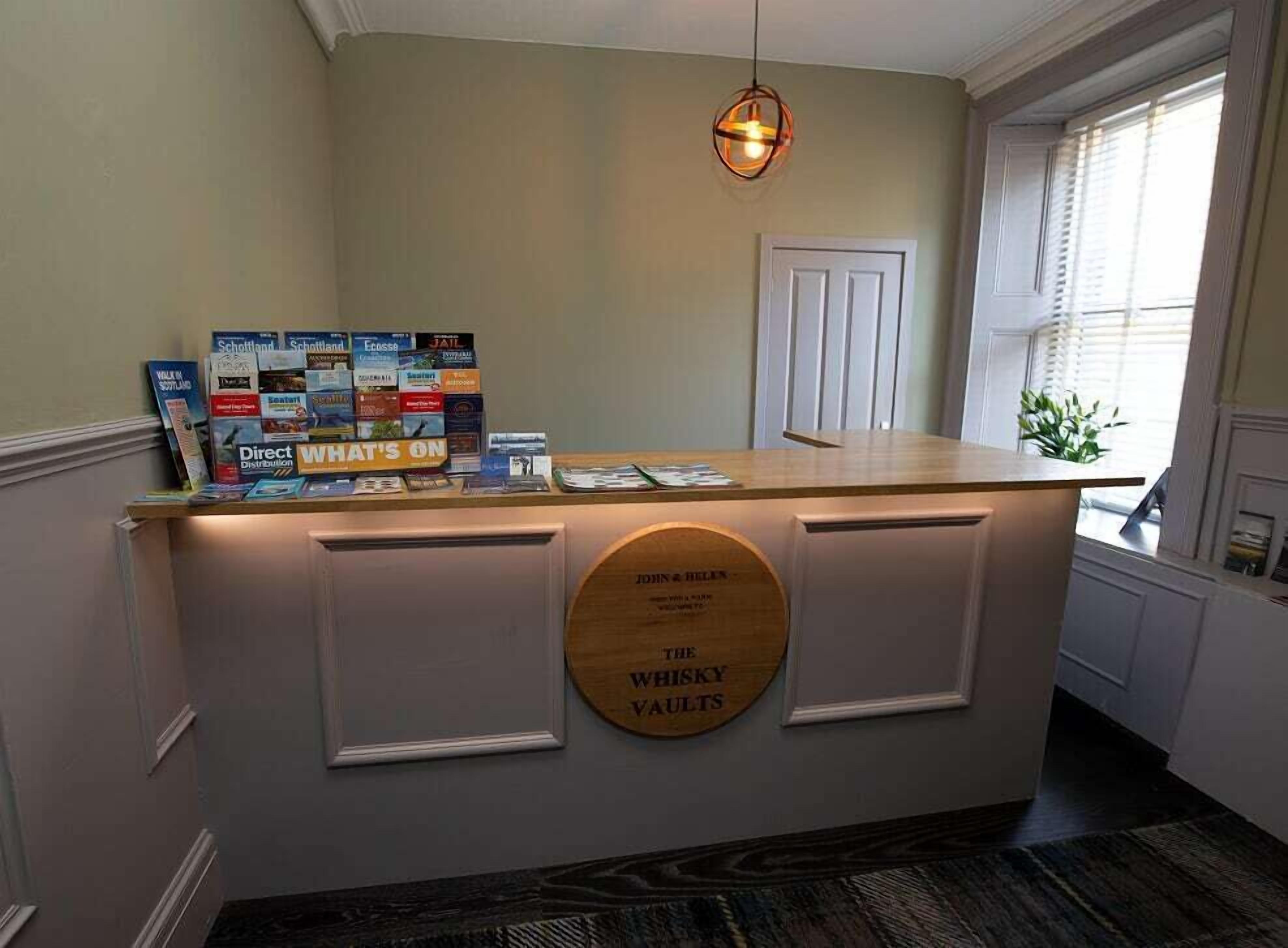 A reception desk with a wooden counter, a sign reading "The Whisky Vaults," and a collection of brochures on the counter.
