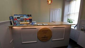 Una mesa de recepción con mostrador de madera, un cartel que dice 'The Whisky Vaults' y una colección de folletos sobre el mostrador.