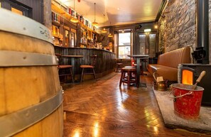 A cozy bar area with wooden barrels, a stone wall, and a fireplace. - The Whisky Vaults (Oban)