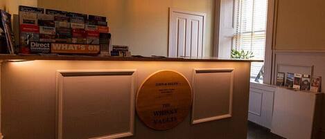 A reception desk with a plaque reading "The Whisky Vaults" and a sign above it listing various whisky brands.
