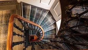 Escadaria em espiral com corrimão de madeira e tapete estampado.