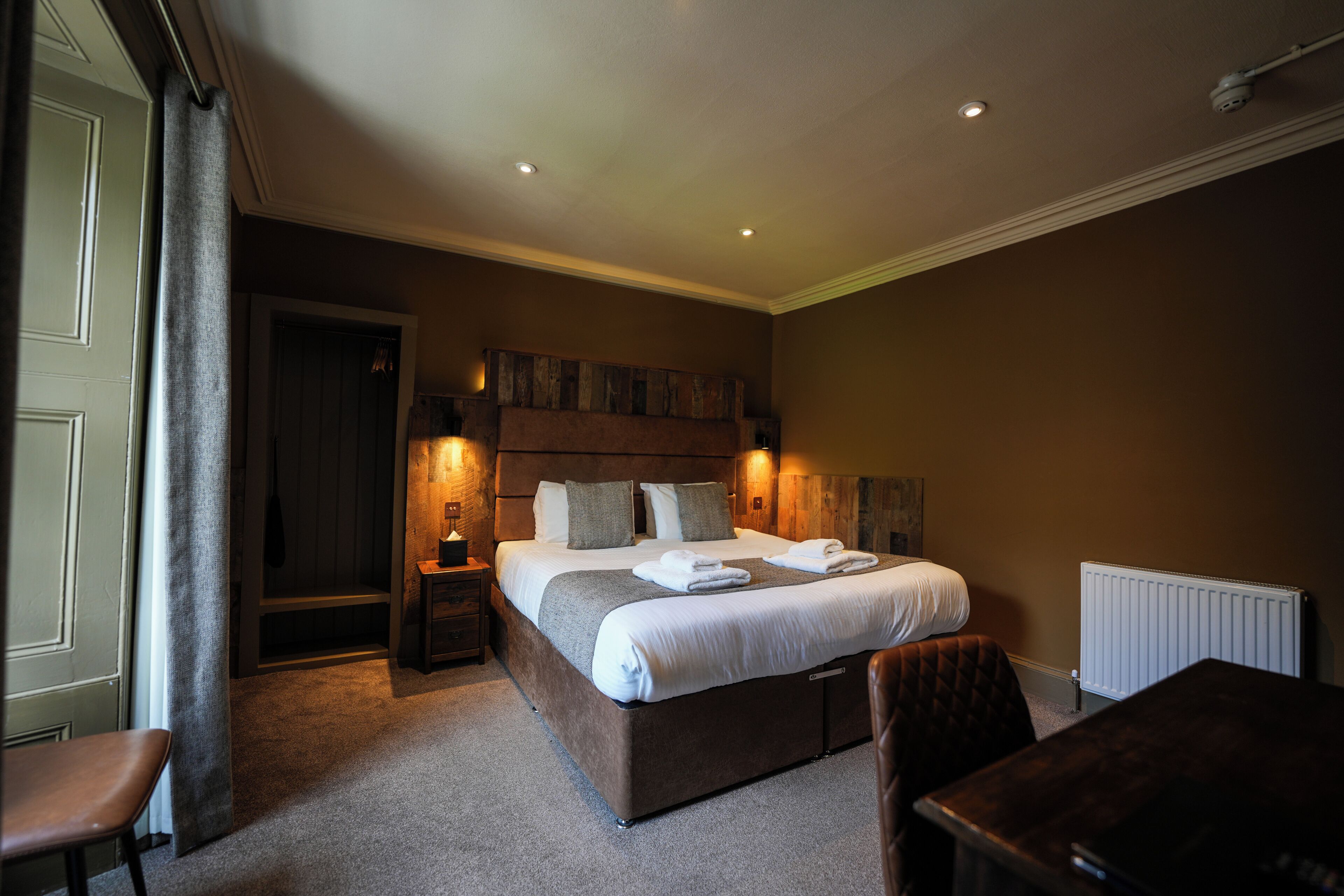 A bedroom with a large bed, bedside tables, a chair, and a radiator.