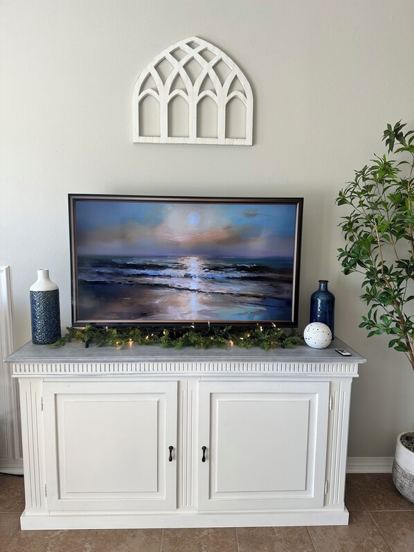 Uma televisão sobre um móvel branco, com um adorno decorativo na parede acima.