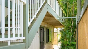 A covered outdoor corridor with a staircase, a door, and a small garden area with plants and flowers. - Quiet & Private S. Kihei 1BR Guest Suite - 10 minute walk to Kamaole Beach II (Kihei)