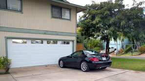 A two-story house with a garage, a black car parked in front, and a tree in the background.