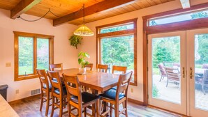 A dining area with a wooden table and chairs, large windows, and a view of the outdoors.