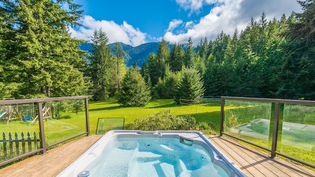 A hot tub on a wooden deck with a view of a grassy area and trees.