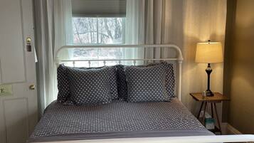 A bed with a white metal frame, dark polka-dotted bedding, and a bedside lamp on a small wooden table.