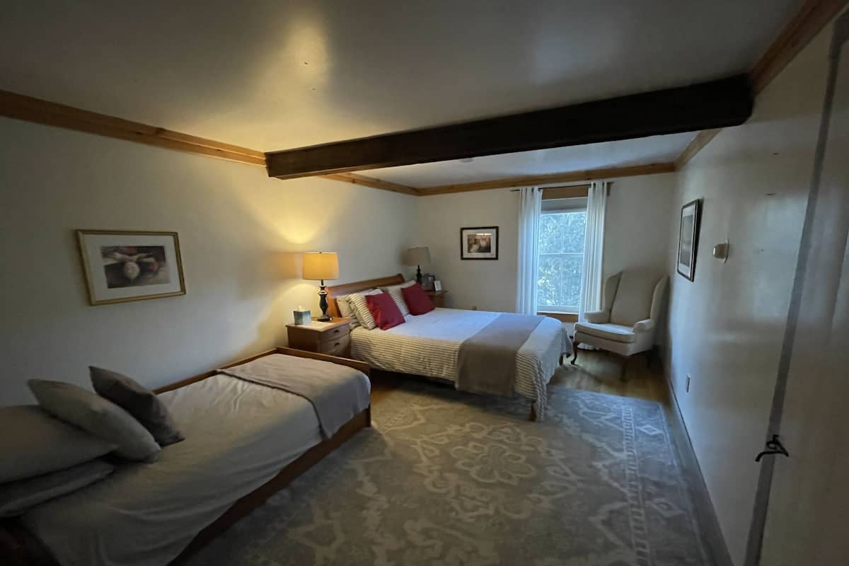 A bedroom with two single beds, a nightstand with a lamp, a chair, and a window with curtains.