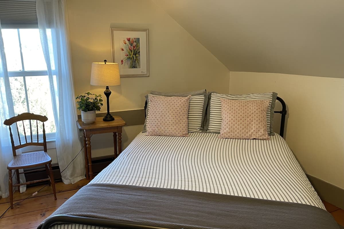 A bedroom with a bed, a chair, a nightstand, a lamp, and a wall-mounted picture.