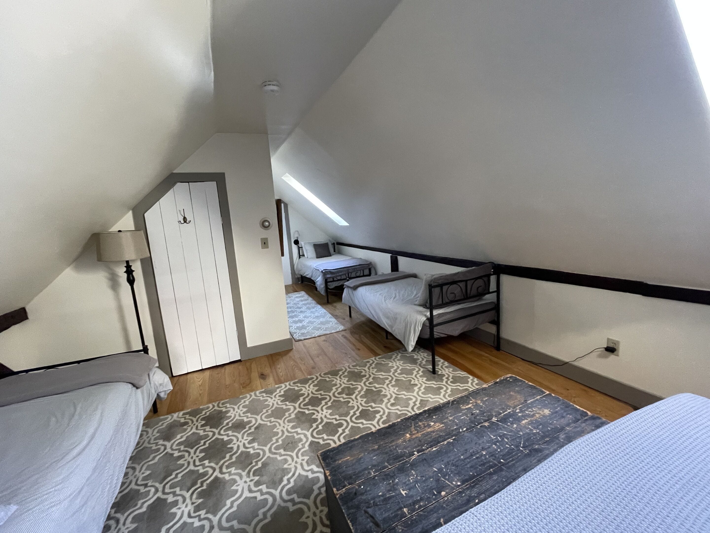A dormitory room with two beds, a desk, a lamp, and a patterned rug.