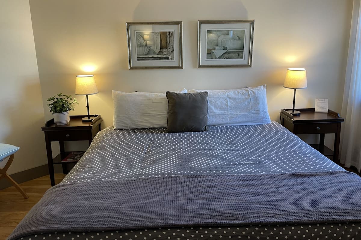 A neatly made bed with a polka dot bedspread and two pillows, flanked by two bedside tables with lamps and framed pictures on the wall above.