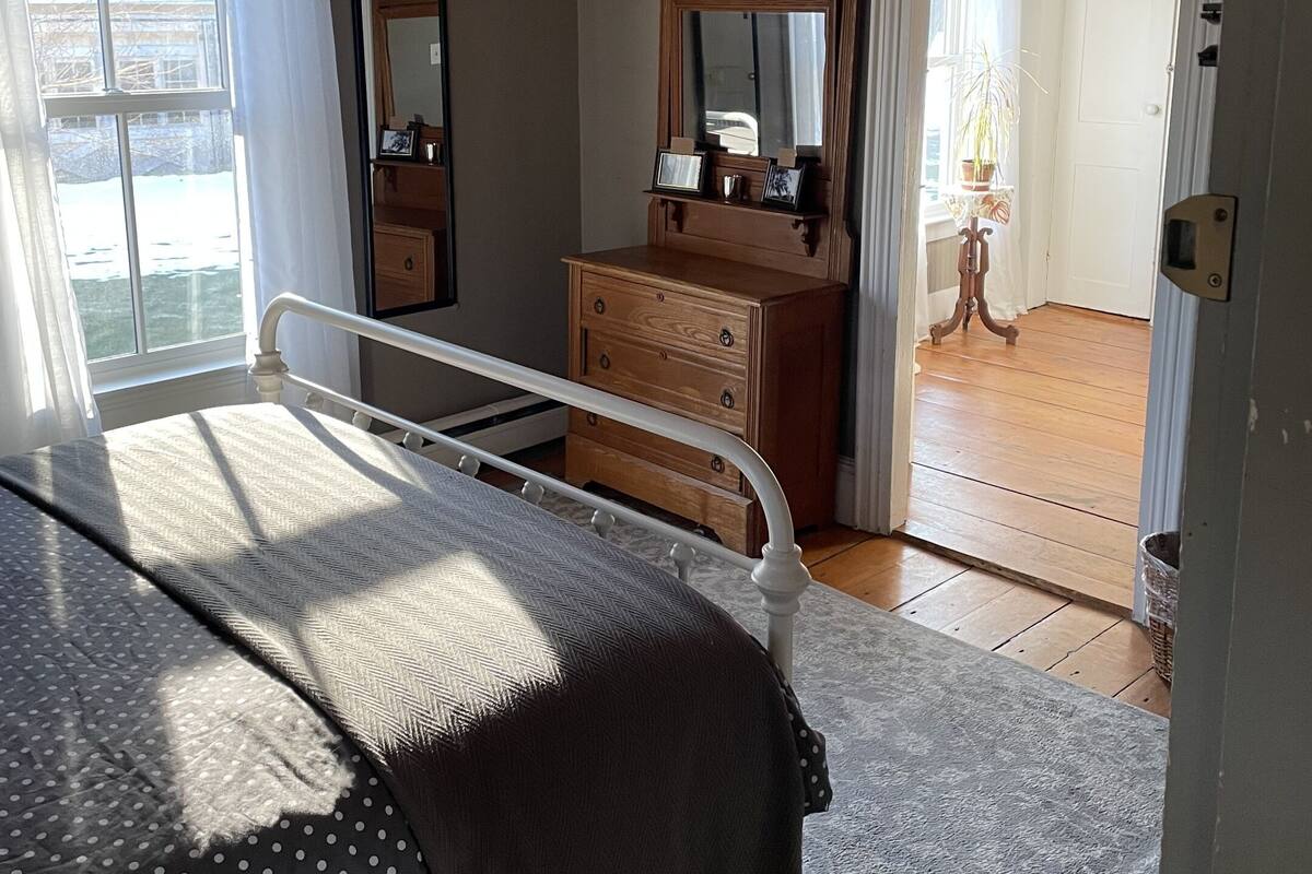 A bedroom with a bed, dresser, mirror, and a door leading to another room.