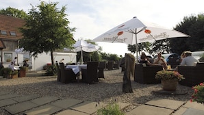 Un espacio de patio al aire libre con mesas, sillas, sombrillas y plantas en macetas.