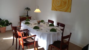 Un comedor con una mesa redonda dispuesta para cuatro personas, rodeada de sillas de madera. Hay una planta en maceta a la izquierda y una lámpara sobre la mesa.