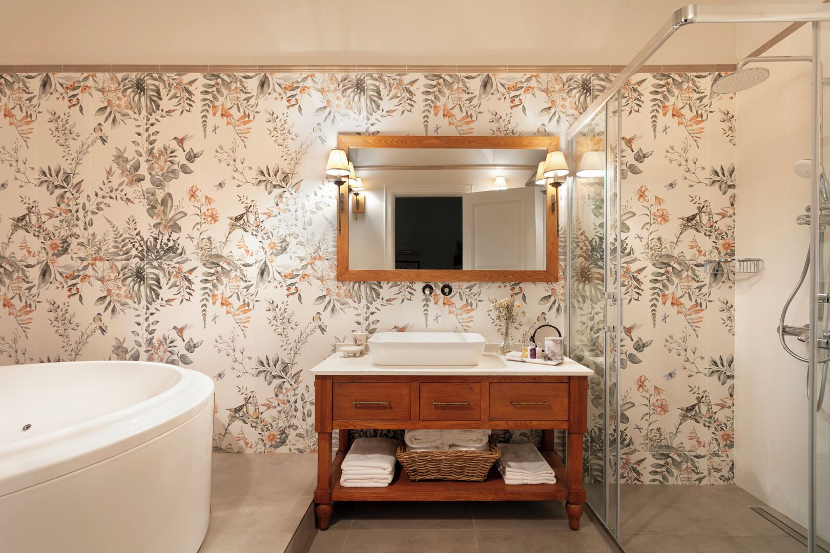 A bathroom with a floral wallpaper, a wooden vanity with a mirror, a white sink, and a bathtub.