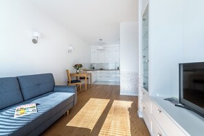 Uma sala de estar moderna com um sofá, uma televisão e uma cozinha ao fundo.