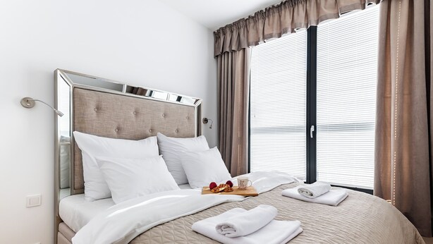 A neatly made bed with white linens, a tray with snacks, and a folded towel on the bed. - P&O Okecie 4 (Warsaw)