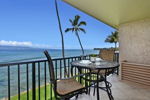 Un balcon avec une table et des chaises donnant sur l’océan, agrémenté d’une petite plante en pot et de verres à vin.