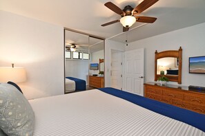 Une chambre à coucher avec un lit, une commode, un miroir et un ventilateur de plafond.