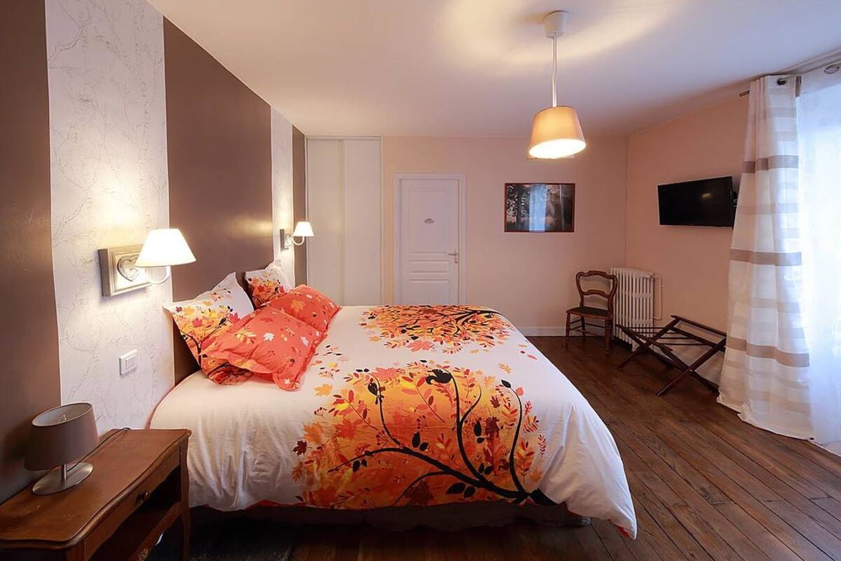 A bedroom with a bed, bedside lamps, a chair, a radiator, and a TV on the wall.