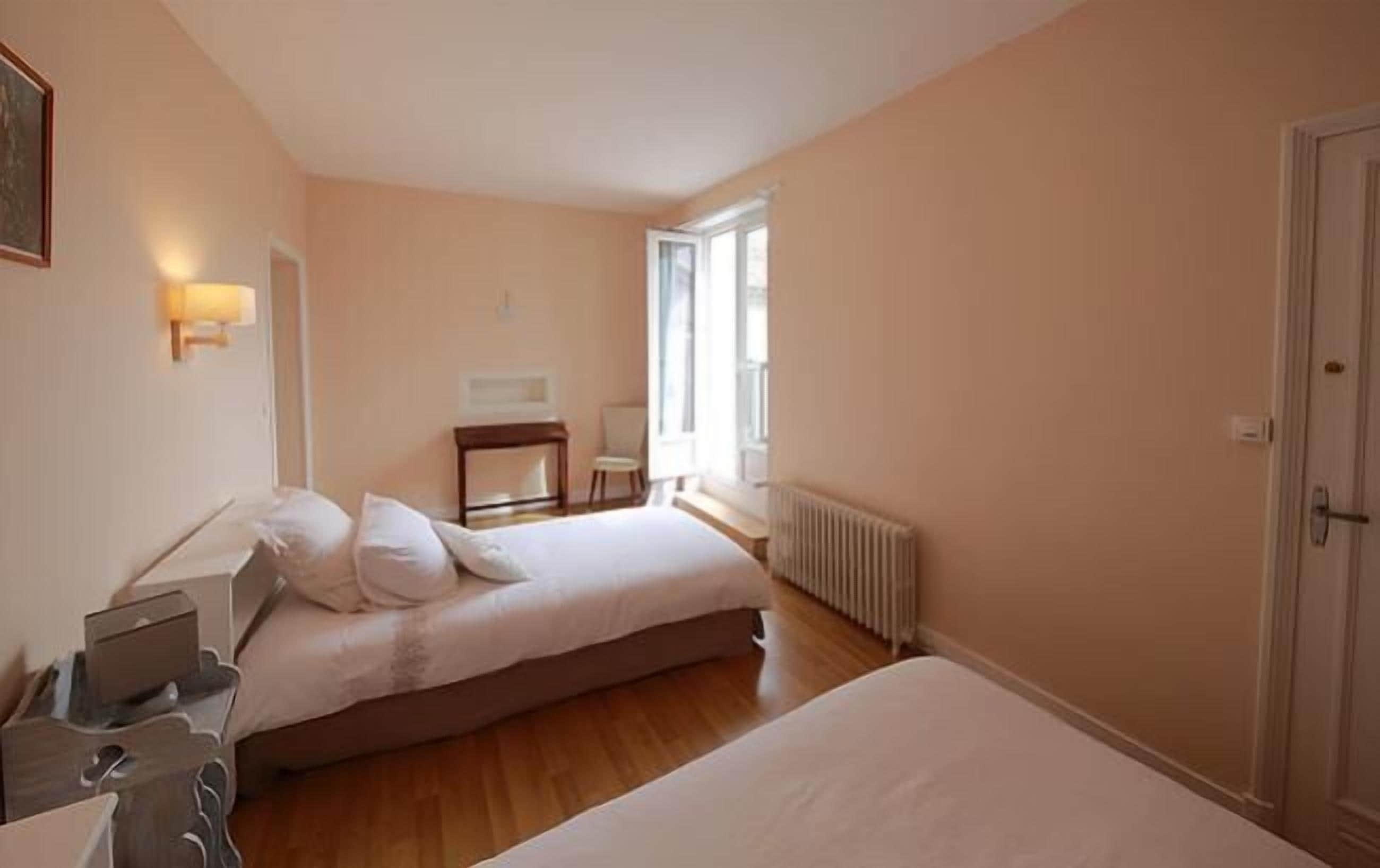 A bedroom with two beds, a bedside table, a chair, and a radiator.