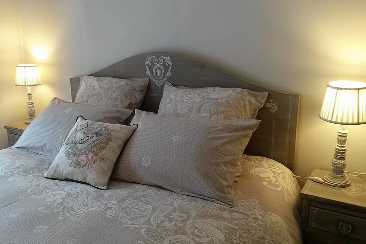 A neatly made bed with a floral-patterned pillow, two matching pillows, and a headboard with a decorative crest. There are two bedside lamps on either side of the bed.
