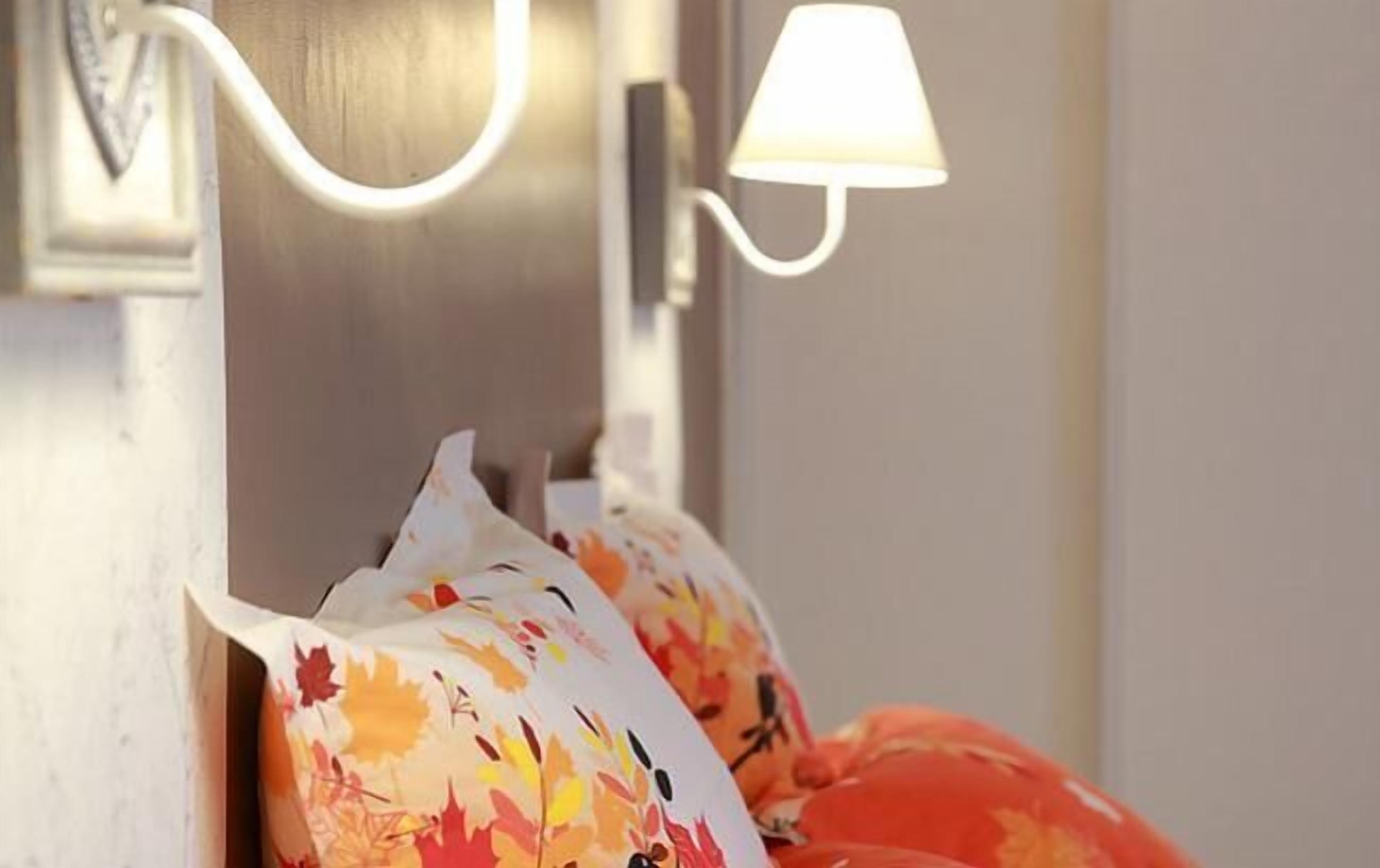 En seng med blomstret sengetøj og en lampe på væggen.