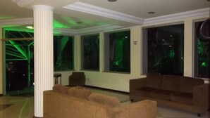 Un hall d’entrée avec une grande colonne blanche, deux canapés et de grandes fenêtres éclairées de lumière verte.