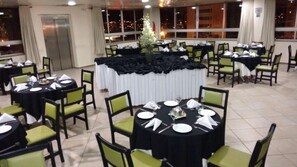 A banquet hall with round tables set for dining, green chairs, and a central decorative black and white draped area. - Hotel Vollare (Osasco)