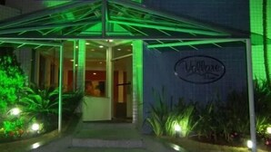 L’entrée d’un hôtel, avec un auvent illuminé de lumière verte et une enseigne bien visible.