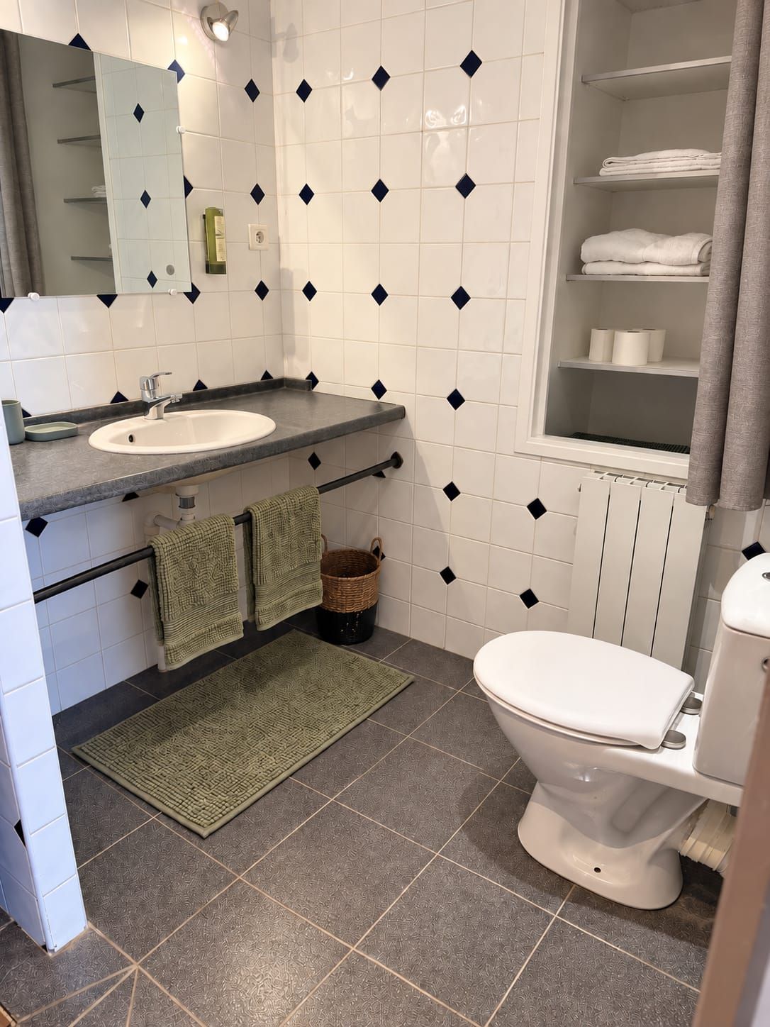 Casa de banho com lavatório branco, sanita, espelho e porta-toalhas.