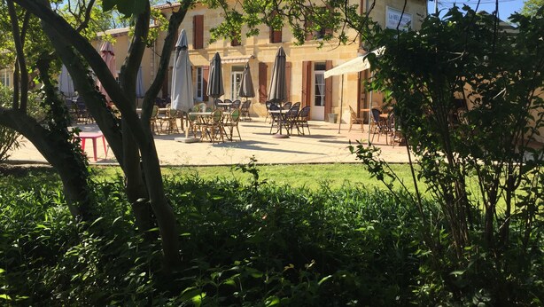 A courtyard with outdoor seating, a building with a sign reading "Le Meliuchop Hotel", and surrounding greenery.