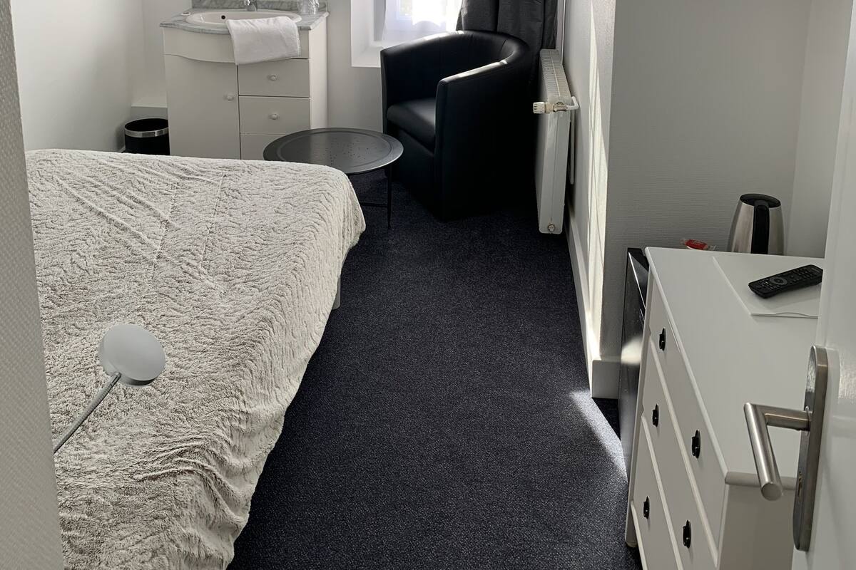 Ein Hotelzimmer mit einem Bett, einem Schreibtisch mit Spiegel, einem Sessel, einem Fernseher und einem Fenster mit Vorhängen.