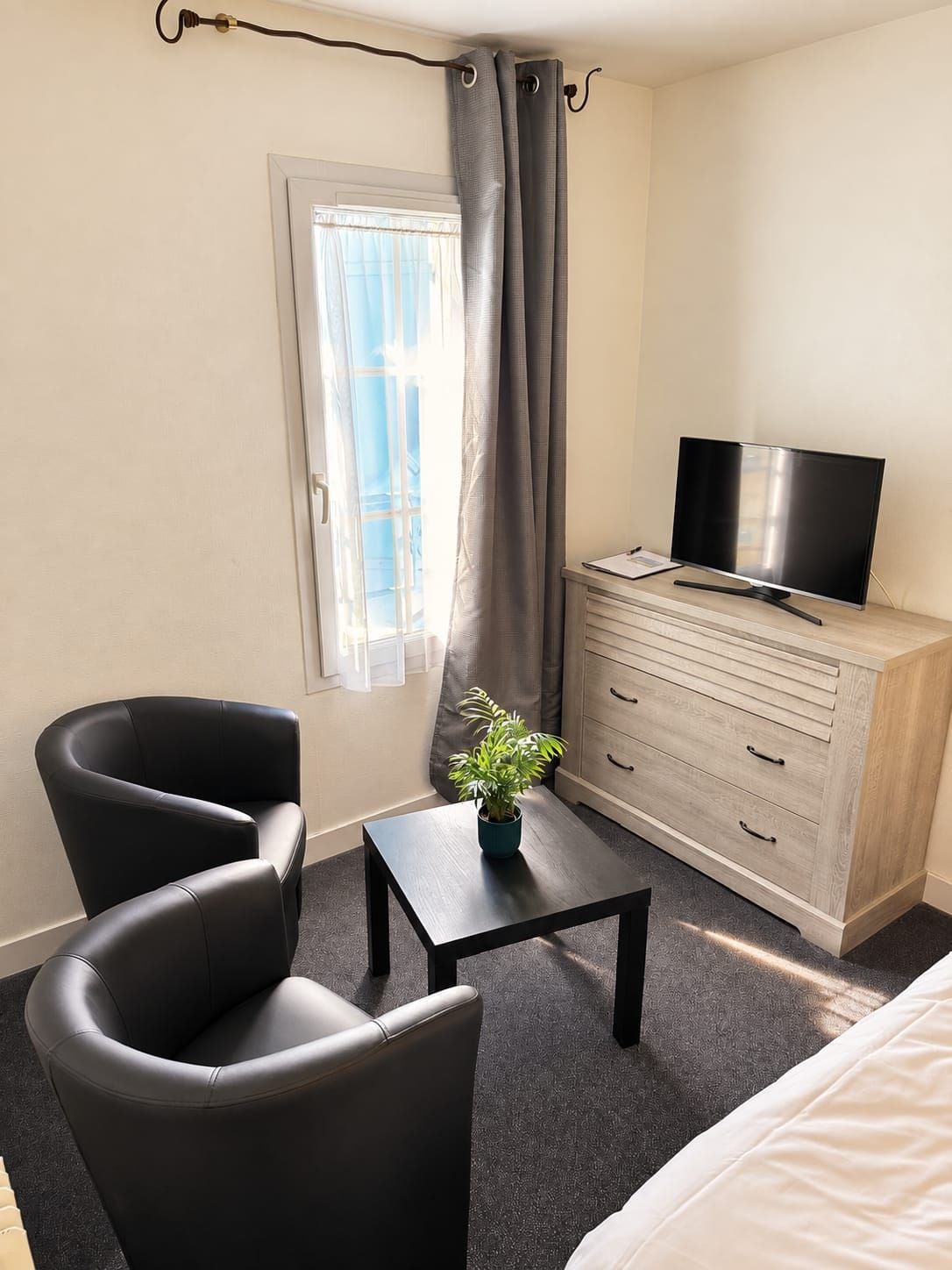 A hotel room with a bed, a desk with a television, a chair, a cabinet, and a window with curtains.