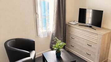 A hotel room with a bed, a desk with a television, a chair, a cabinet, and a window with curtains.