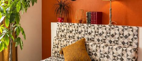 Ein modernes Wohnzimmer mit einem sofa mit geometrischem Muster, einem Topfpflanzen, einer Lampe und dekorativen Spiegeln an der Wand.