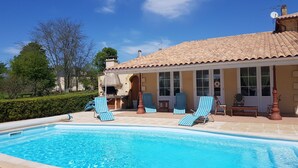 A swimming pool with lounge chairs, a covered patio, and a building with a tiled roof.