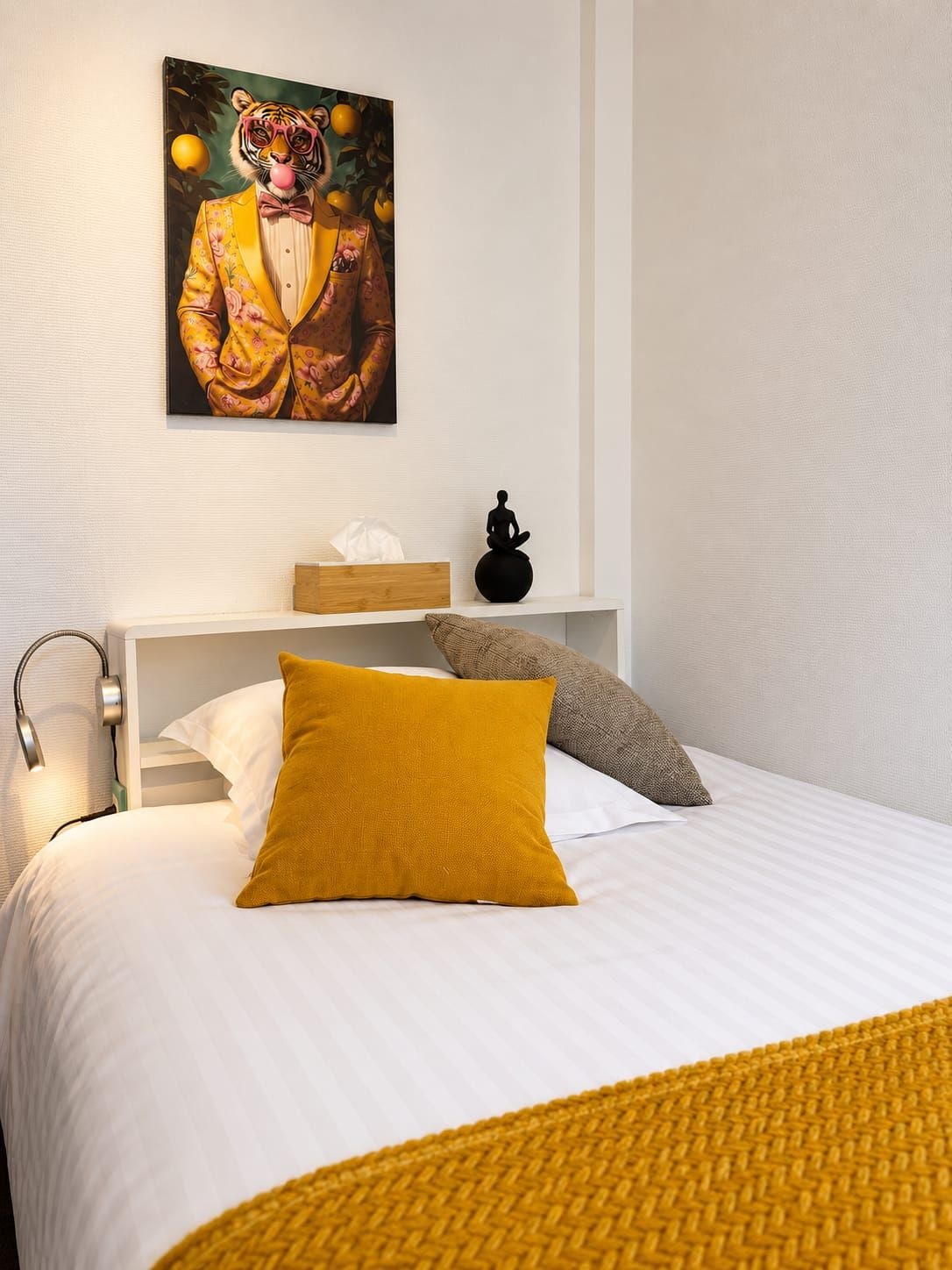 A bedroom with a bed, a painting of a tiger, a small statue, and a bedside lamp.