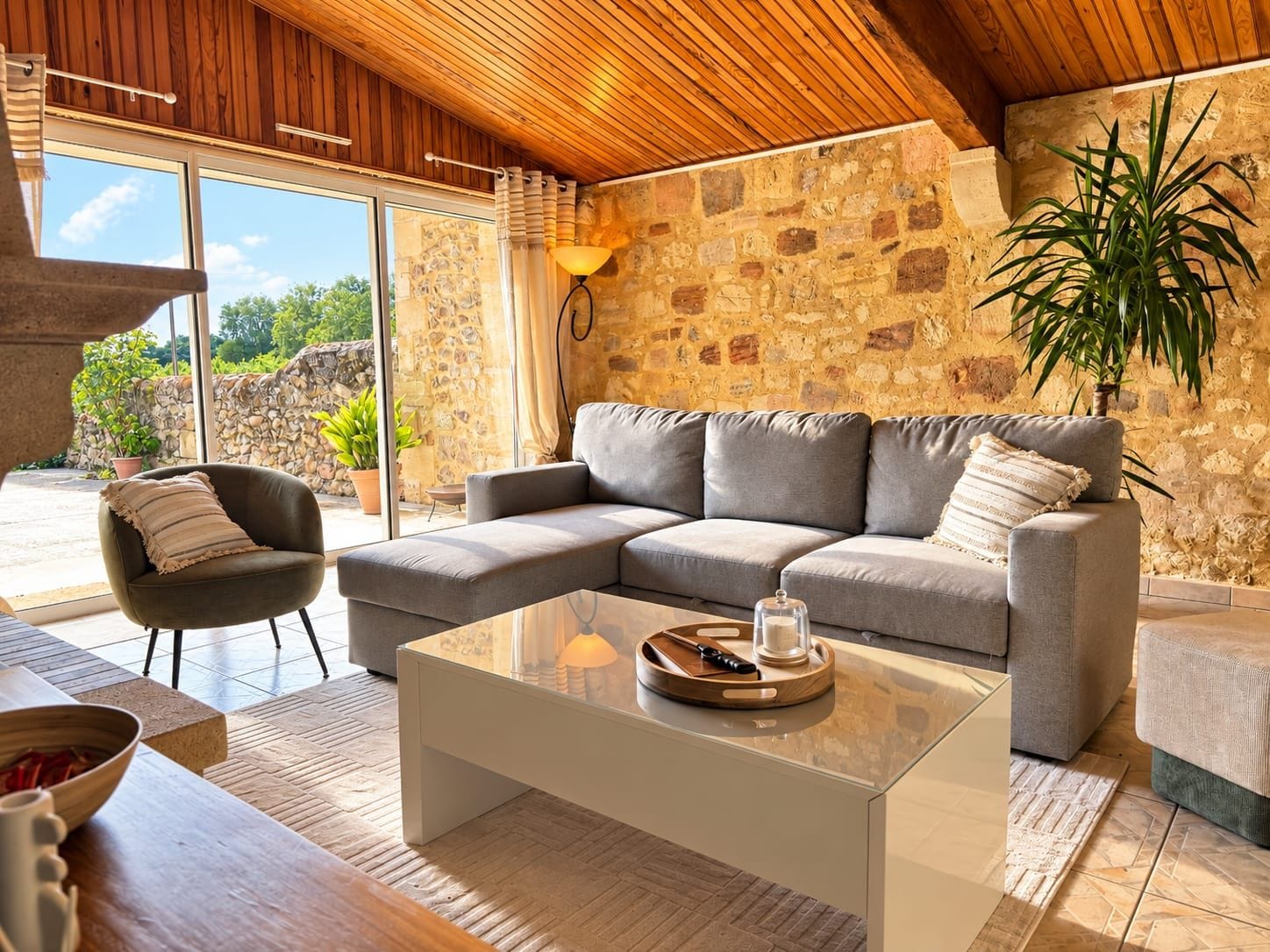 A modern living room with a stone wall, a grey sofa, a wooden coffee table, and a potted plant.